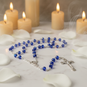 Glass Birthstone Rosary for September on a white surface with lit candles in the background