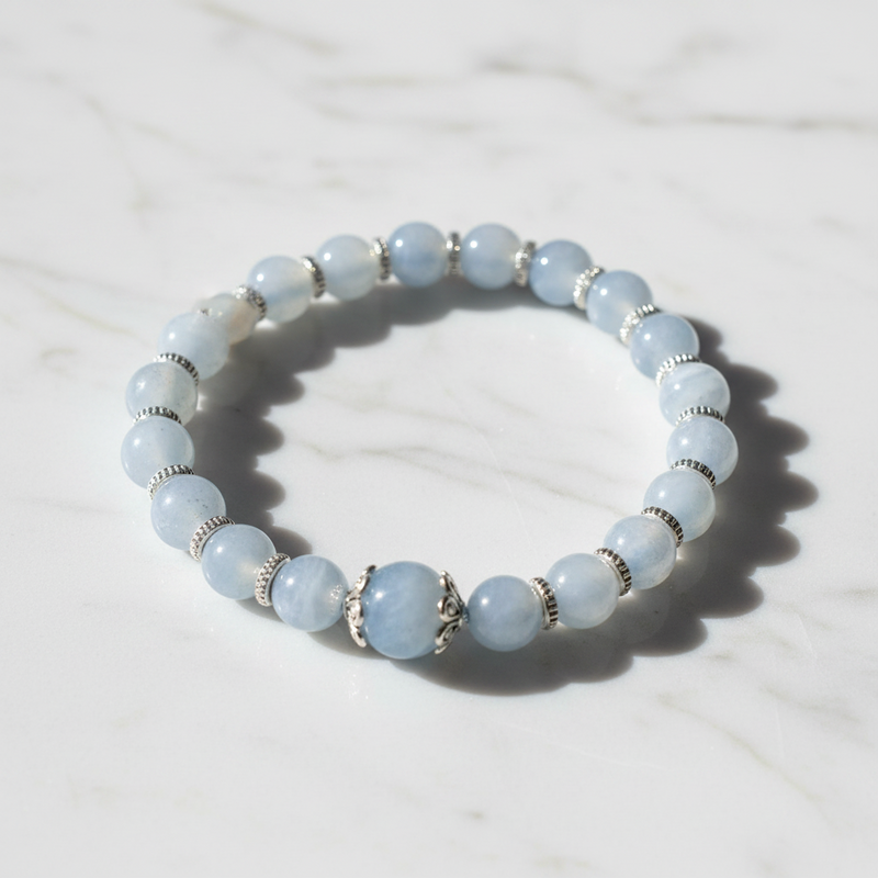 A beaded stretch bracelet made of light blue round beads with silver-toned spacer rings and a central decorative silver bead, displayed on a white marble surface.