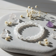 A beaded stretch bracelet made of translucent milky white round beads, styled on a light gray stone with dried flowers and clear crystals.