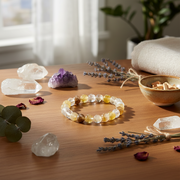 A beaded bracelet made of clear and yellow translucent stones sits on a wooden table surrounded by crystals, dried lavender, a small bowl, and soft natural light.
