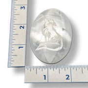Selenite palm stone  with engraved wolf design next to a ruler for scale on a white background