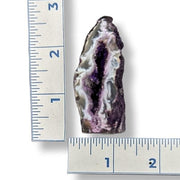Geode with purple and white interior next to a ruler for scale on a white background