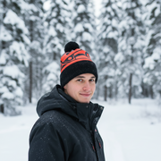 Person wearing a black and orange beanie in a snowy forest