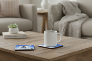 A white ceramic mug sits on a square coaster on a wooden coffee table, with steam rising from the cup. A second coaster with a blue and white graphic design lies nearby.