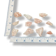 Raw rose calcite on a white background with a ruler for scale