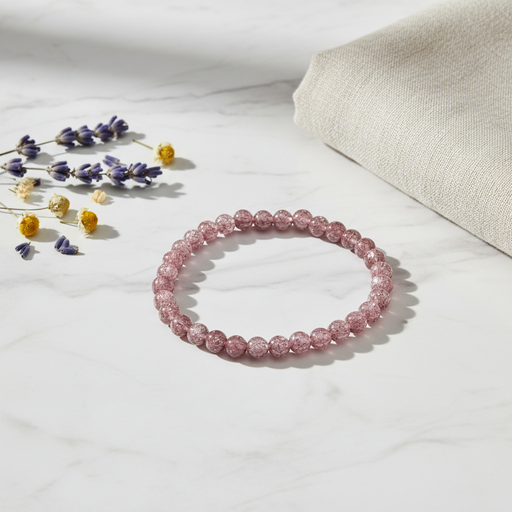 A pink beaded bracelet made of faceted round beads, styled on a white marble surface with dried lavender sprigs and a folded beige linen cloth.