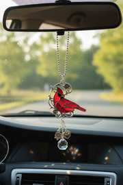 A red cardinal bird car car charm  hanging from a silver ball chain and mirror clip, displayed inside a car dashboard.