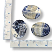 Three sodalite worry stones of varying sizes, with deep blue coloring and natural calcite inclusions, displayed next to a ruler for size comparison.