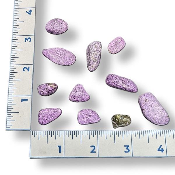 A collection of polished tumbled stitchite gemstones of varying sizes, placed on a surface with a measuring tape for scale.