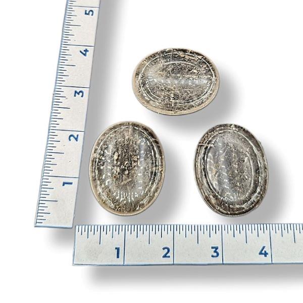 Three smokey quartz worry stones of varying sizes, placed on a white surface, with a ruler for scale.