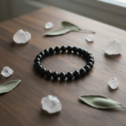 Black beaded bracelet on a wooden surface with crystals and leaves