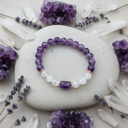 Purple beaded bracelet on a white stone surrounded by crystals and lavender flowers