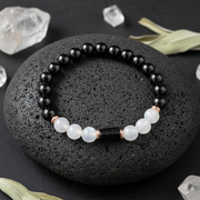 Black and white beaded bracelet on a dark stone surface with crystals around