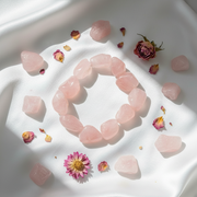 Rose quartz bracelet on a white fabric background with scattered rose petals and flowers.