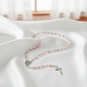 Pink pearl rosary  with a cross on a white cloth surface