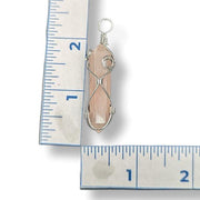 Crystal pendant with silver wire wrapping next to a ruler for scale on a white background