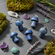 Blue mushroom-shaped pendants on a dark surface with crystals and herbs
