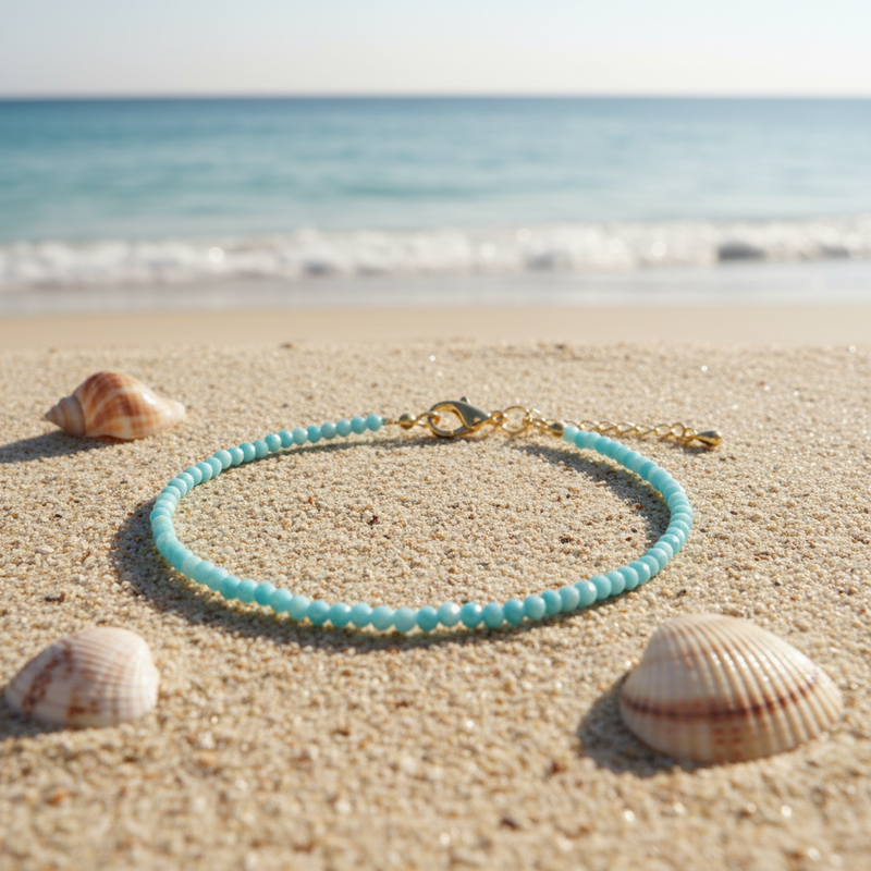 Turquoise beaded anklet on sand with shells and ocean in the background