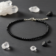 Black beaded anklet on a dark surface with crystals around