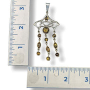Decorative pendant with beads next to a ruler for scale on a white background