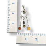 Silver pendant with colored stones next to a ruler for scale on a white background