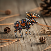 Decorative moose pin on a wooden surface with pine cones
