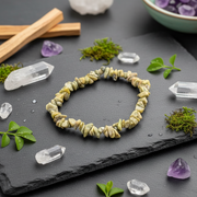 A beige bracelet on a grey background surrounded by herbs and crystals