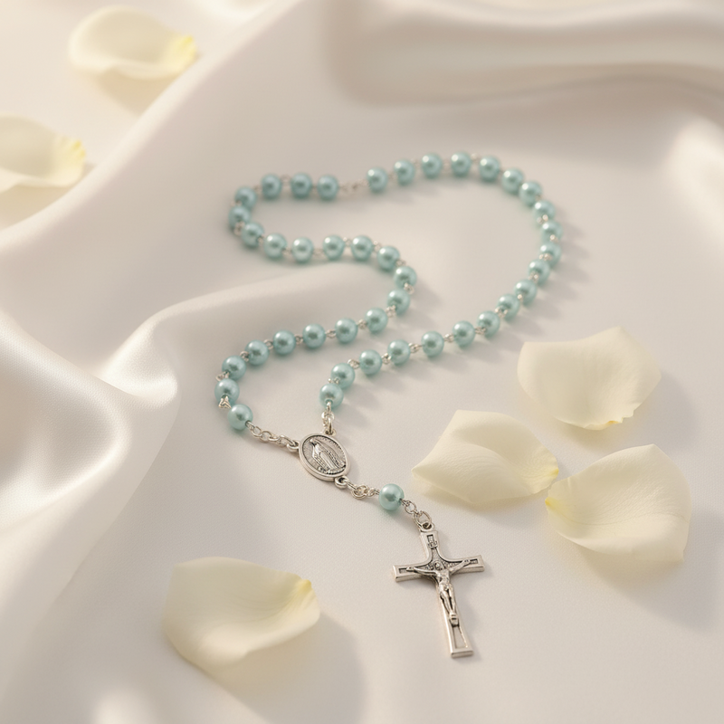 light blue rosary with silver cross on a white fabric background with rose petals
