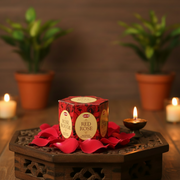 Red Rose incense box with red rose petals on a wooden stand with candles and plants in the background