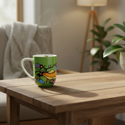 A green ceramic mug with a colorful  design sits on a wooden table in a cozy living room setting with a sofa, lamp, and plant in the background.