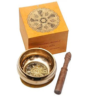 Brass singing bowl with decorative patterns, wooden stick, and gift box on a white background
